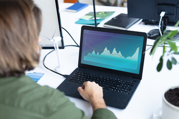 Caucasian businesswoman sitting at desk, using laptop with statistical data on screen