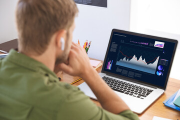 Caucasian businessman sitting at desk, using laptop with statistical data on screen