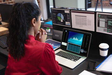 Fototapeta na wymiar Biracial businesswoman sitting at desk, using laptop with statistical data on screen