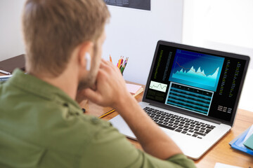 Caucasian businessman sitting at desk, using laptop with statistical data on screen