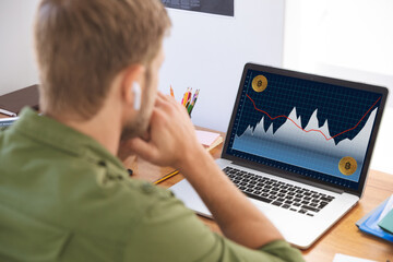 Caucasian businessman sitting at desk, using laptop with statistical data on screen