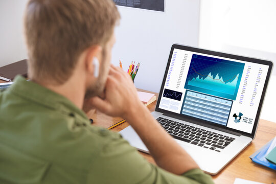 Caucasian businessman sitting at desk, using laptop with statistical data on screen