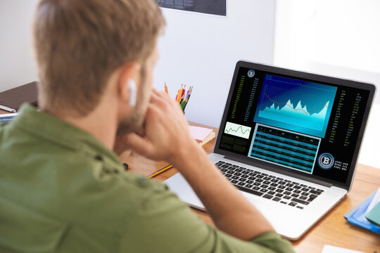 Caucasian businessman sitting at desk, using laptop with statistical data on screen