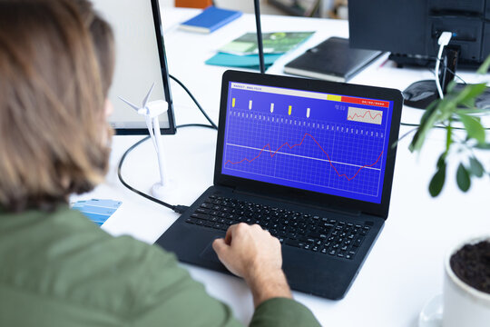 Caucasian businesswoman sitting at desk, using laptop with statistical data on screen