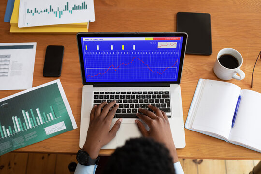 Hands of african american businessman sitting at desk, using laptop with statistical data on screen