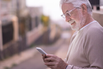 Portrait of attractive  senior man standing outdoors at sunset using mobile phone. Attractive elderly retiree using technology