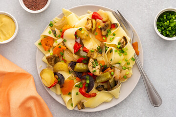 Fettuccine pasta with stewed vegetables, delicious autumn lunch in plate with mustard and fresh green onions