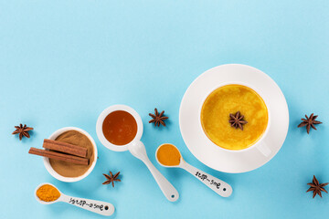 Turmeric golden milk latte with spices, cinnamon and honey on blue background. Healthy traditional...
