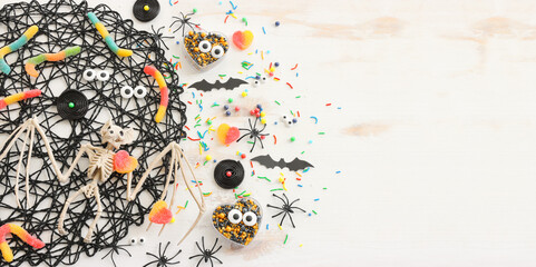 top view image of Halloween holoday. witcher broom, treats, spiders and bats over white wooden table