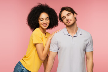 Fototapeta premium curly hispanic woman leaning on shoulder of young man looking at camera isolated on pink.
