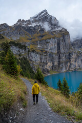 Man with yellow jacket at Oeschinensee mountain lake in the alps of Switzerland in a cloudy day