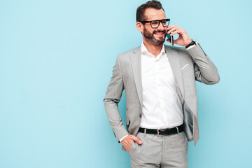 Portrait of handsome smiling stylish hipster lambersexual model.Sexy modern man dressed in elegant suit. Fashion male posing in studio near blue wall. Talking at smartphone. Speaking at phone