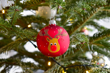 Red Christmas ball with a Rudolf reindeer drawing on it in the Christmas tree. 