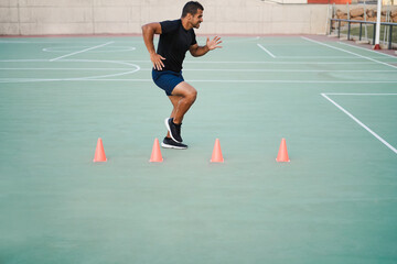 Hispanic man doing speed and agility cone drills workout session outdoors - Focus on man face