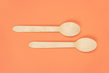 Eco-friendly disposable tableware made of bamboo. Two wooden disposable spoons on orange background, close up
