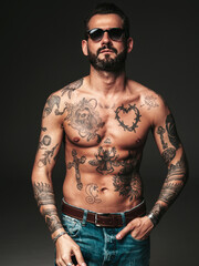 Fototapeta premium Portrait of handsome confident stylish hipster lambersexual model. Sexy modern man. Naked torso with tattoos.Fashion male posing in studio on dark background in sunglasses