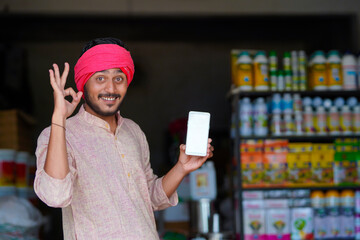 Indian farmer showing smartphone at fertilizer shop. - obrazy, fototapety, plakaty
