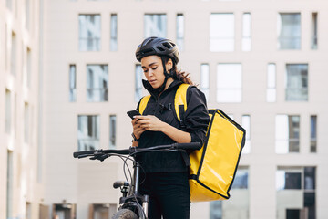 Woman courier with backpack checking information for delivery in the city - obrazy, fototapety, plakaty