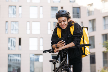Portrait of a beautiful delivery girl holding her mobile phone while leaning on a handlebar of a bicycle - Powered by Adobe