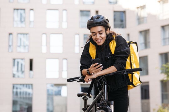 Portrait of a beautiful delivery girl holding her mobile phone while leaning on a handlebar of a bicycle