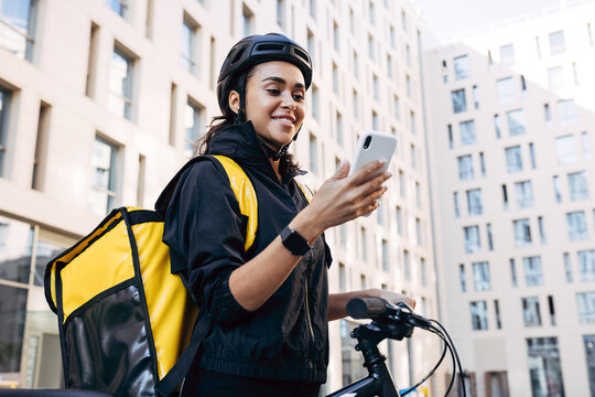 Beautiful young woman working as a courier with a delivery bag on her back, holding mobile phone and smiling