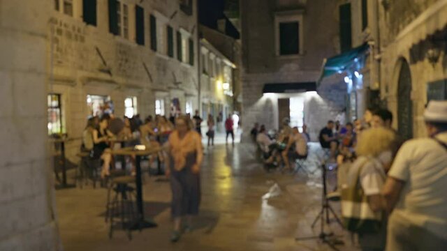 Defocused shot of people walk on summer evening in old center of European town. Street cafes with visitors, communication, rest. Cozy romantic atmosphere