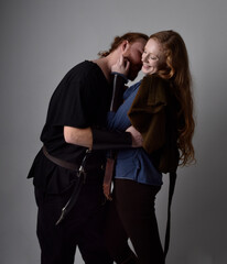 Full length  portrait of red haired  couple, man and woman wearing medieval viking inspired fantasy costumes, standing romantic intimate poses, isolated on white  studio background.