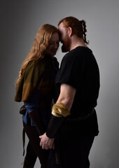 Full length  portrait of red haired  couple, man and woman wearing medieval viking inspired fantasy costumes, standing romantic intimate poses, isolated on white  studio background.