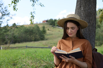 Young woman reading book under tree on meadow