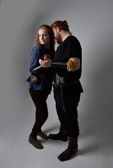 Fototapeta na wymiar Full length portrait of red haired couple, man and woman wearing medieval viking inspired fantasy costumes, standing romantic intimate poses, isolated on white studio background.