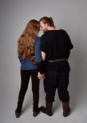 Full length  portrait of red haired  couple, man and woman wearing medieval viking inspired fantasy costumes, standing romantic intimate poses, isolated on white  studio background.