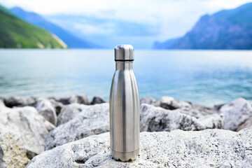 Steel eco thermo water bottle on the background of the lake in the mountains.  Clean and healthy...