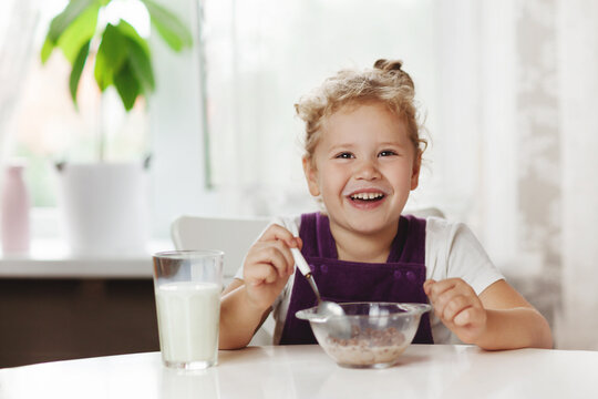 Charming girl eats cereal with milk for Breakfast and . On the table are chocolate flakes, a glass of milk. Healthy Breakfast, taking care of children. Space for text