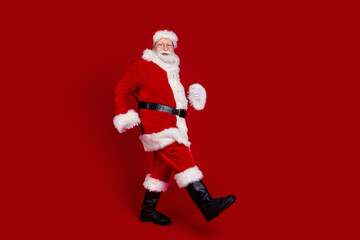 Fototapeta na wymiar Photo of cute funky man pensioner dressed santa claus costume boots walking empty space smiling isolated red color background