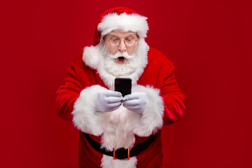 Photo of funky impressed man pensioner dressed santa claus costume chatting modern device big eyes isolated red color background