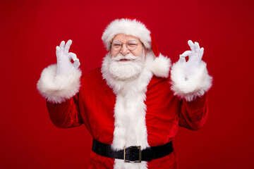 Photo of confident handsome man pensioner dressed santa claus costume showing okey signs smiling isolated red color background