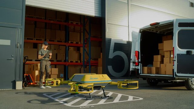 Storage Facility Female Employee Uses Tablet Computer to Send Autonomous Flying Delivery Drone with a Parcel. Futuristic Parcel Drone Takes Off on Flight from Warehouse to Client Waiting for Package