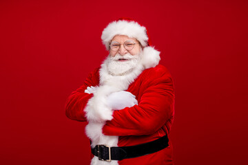 Photo of handsome confident man pensioner dressed santa claus costume taarms folded smiling isolated red color background