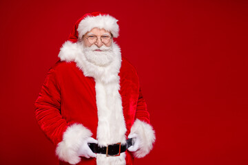 Photo of positive cheerful retired man wear santa claus costume coat fur belt spectacles smiling arms hands waist isolated red color background