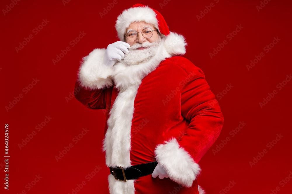 Wall mural Photo of funky positive retired man wear santa claus costume belt spectacles smiling arm mustaches isolated red color background