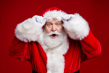Photo of amazed surprised retired man wear santa claus costume arms spectacles open mouth isolated red color background