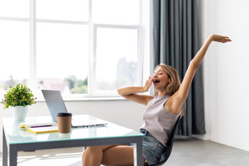 young businesswoman with legs on the table stretches her hands and yawn in office - obrazy, fototapety, plakaty