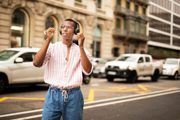Cheerful guy with the headphones. Young african man listening the music outdoors.