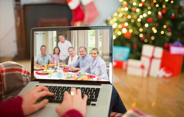 Caucasian woman making christmas laptop video call with smiling multi generation family at table