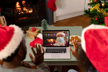 Waving african american couple making laptop christmas video call with santa claus in face mask