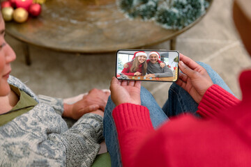 Smiling diverse couple making smartphone christmas video call with embracing caucasian couple