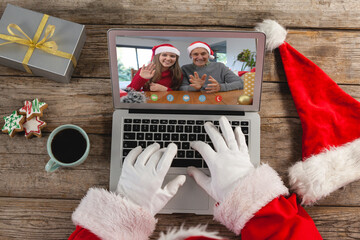 Santa claus making laptop christmas video call with waving caucasian father and daughter