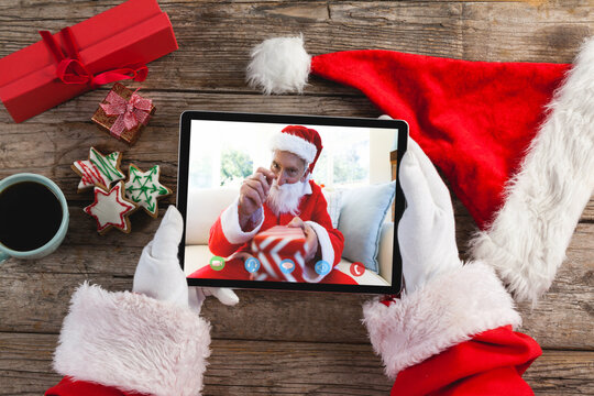 Santa claus making tablet christmas video call with waving caucasian senior man in santa costume