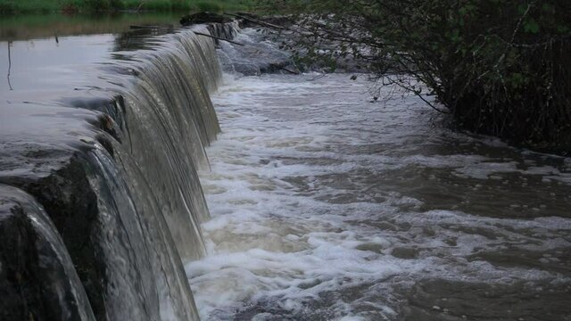 Keravanjoki river water flowing in slow motion over small dam with trout jumping while migrating towards spawning areas on rainy early October evening in Vantaa, Finland (original file).