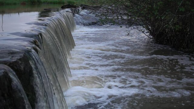 Keravanjoki river water flowing in slow motion over small dam with trout jumping while migrating towards spawning areas on rainy early October evening in Vantaa, Finland (original file).